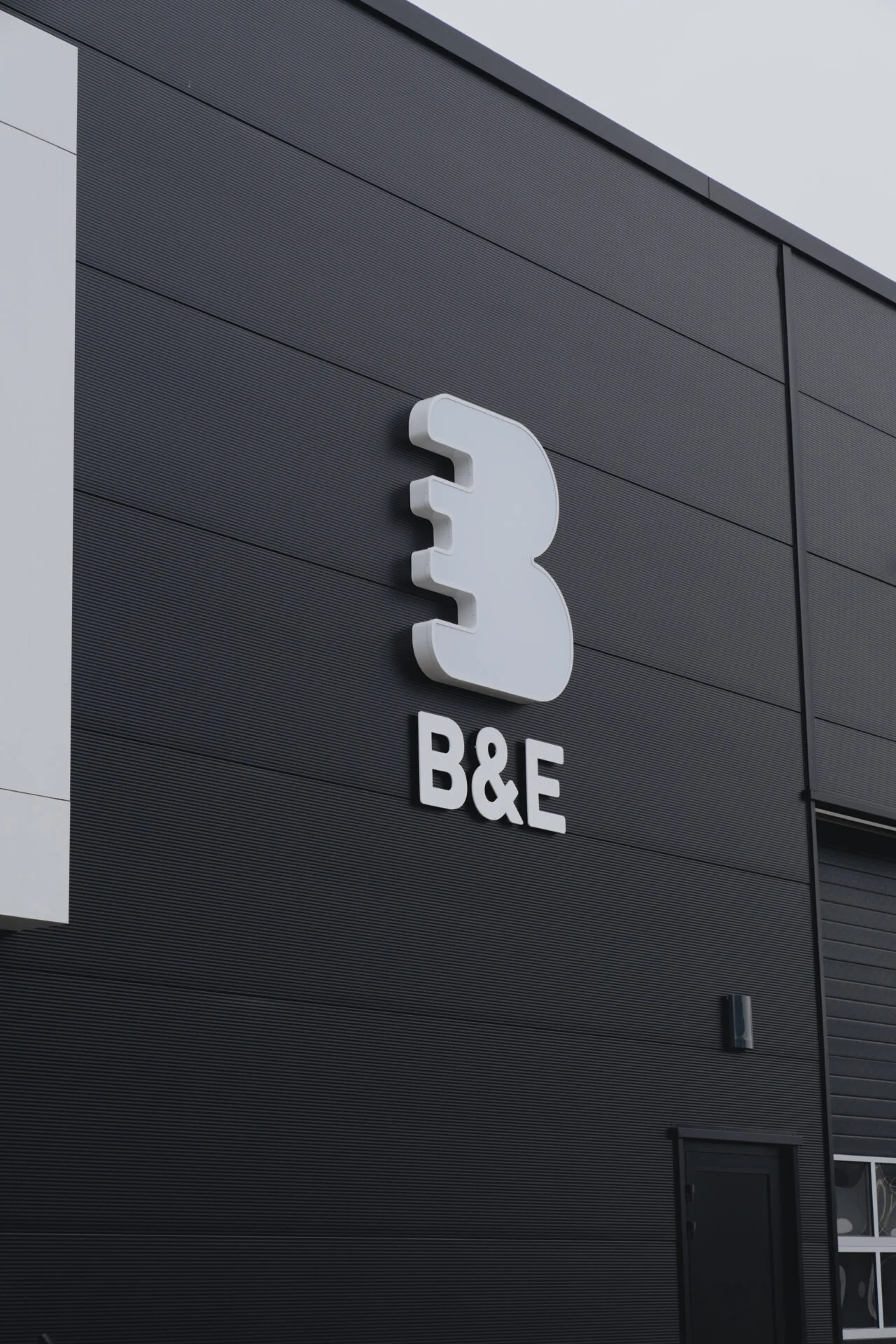 Gevelreclame B&E met losse witte letters op donkere bedrijfsgevel